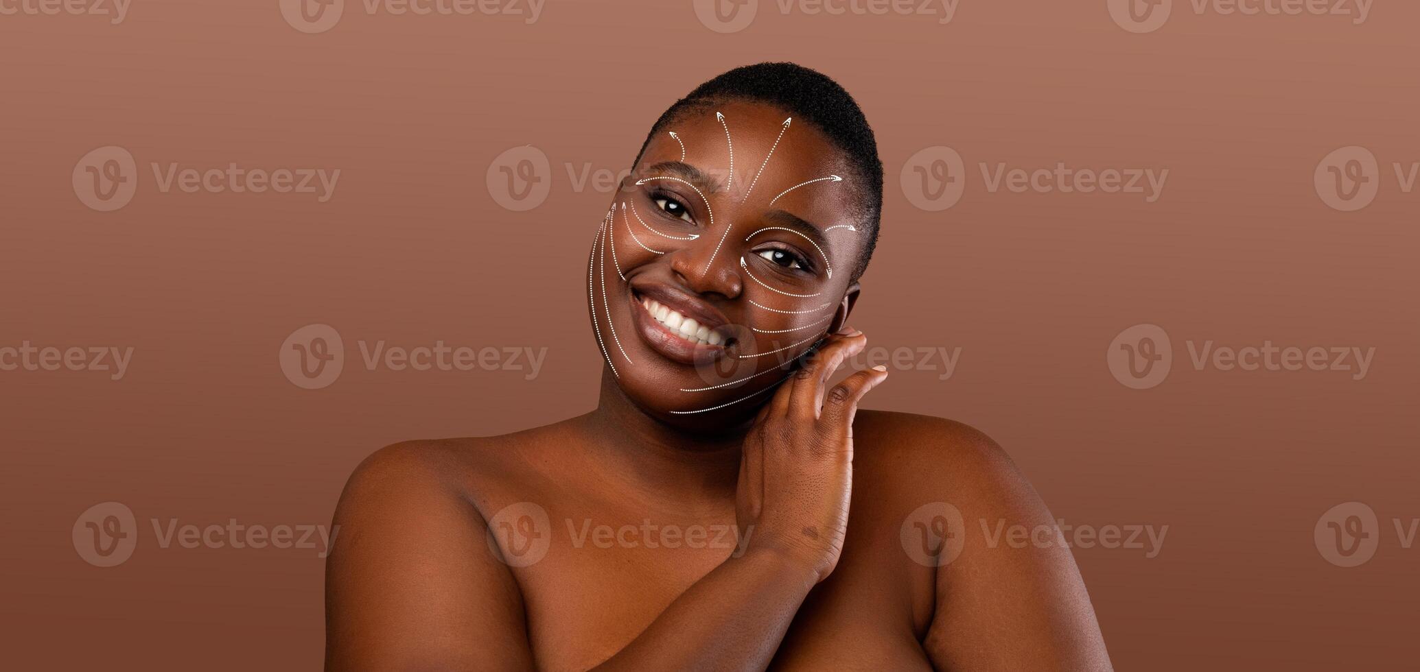 African American woman engages in her skin care routine, smiling as she pampers herself. Her skin is adorned with a unique design, showcasing her beauty in a serene, isolated environment. photo