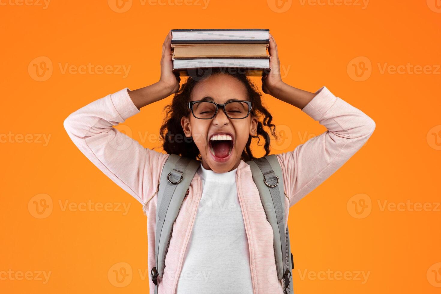 A Lot Of Homework. Portrait of tired black student girl putting and holding pile of academic books on her head and screaming, wearing eyeglasses and backpack, yellow color studio background photo