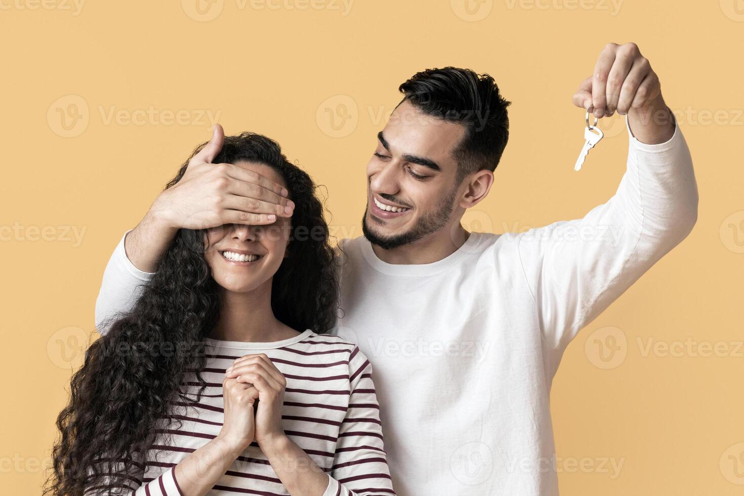 Smiling Arab Man Holding Home Keys And Surprising His Excited Girlfriend, Cheerful Young Middle Eastern Couple Buying New House, Standing Together Over Yellow Studio Background, Copy Space photo