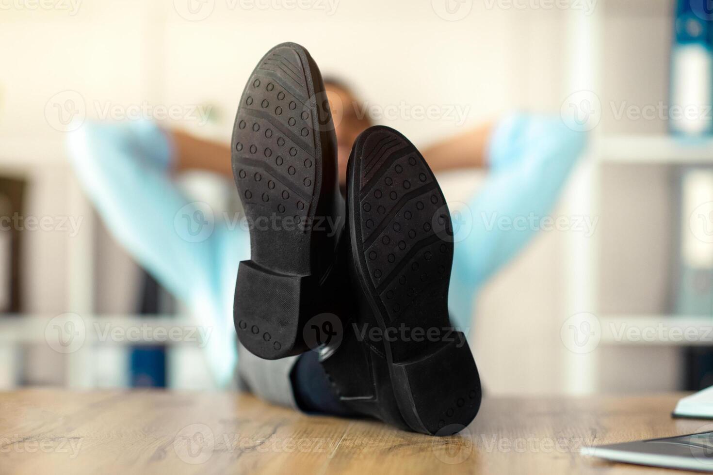 Millennial Arab office employee relaxing after work, putting legs on table at workplace, focus on feet. Young entrepreneur resting with hands behind his head, taking break from job photo
