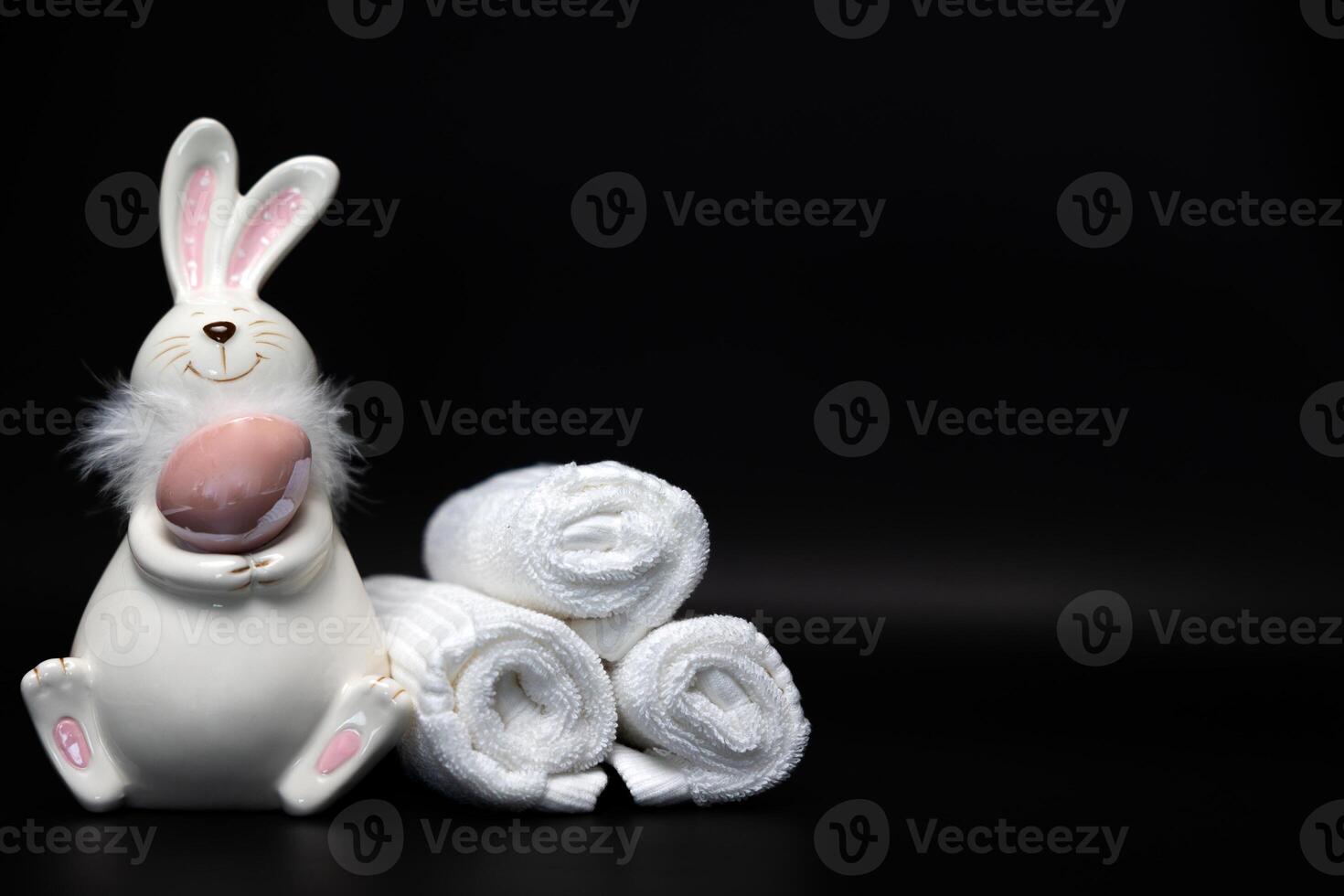 Easter white bunny with a brown egg on a black background with white spa towels photo