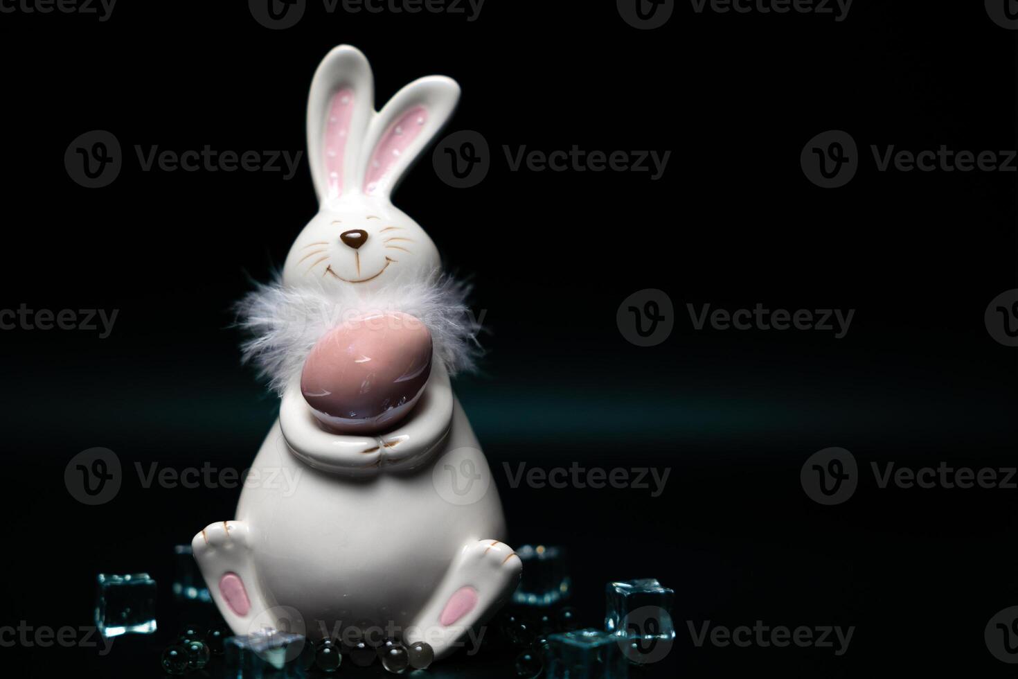 Sculpture of a white rabbit with Easter eggs on black background with ice cubes photo