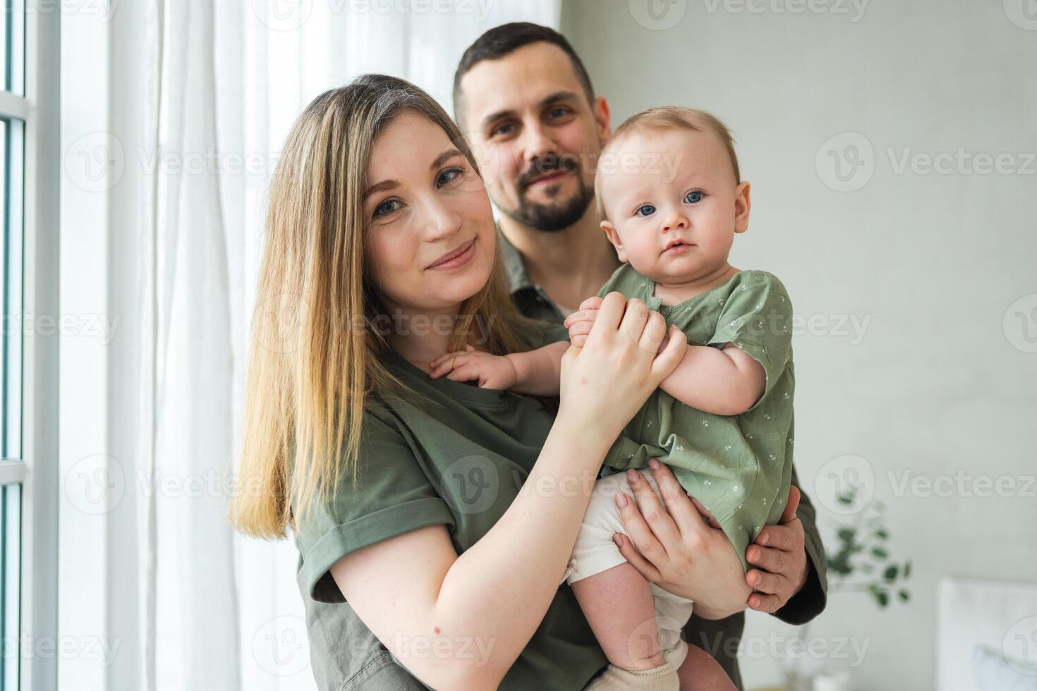 Happy family at home. Mother father holding little toddler child. Mom dad baby girl relax playing having fun together. Woman man hugging embracing baby with love care. Parent of breast feeding baby photo
