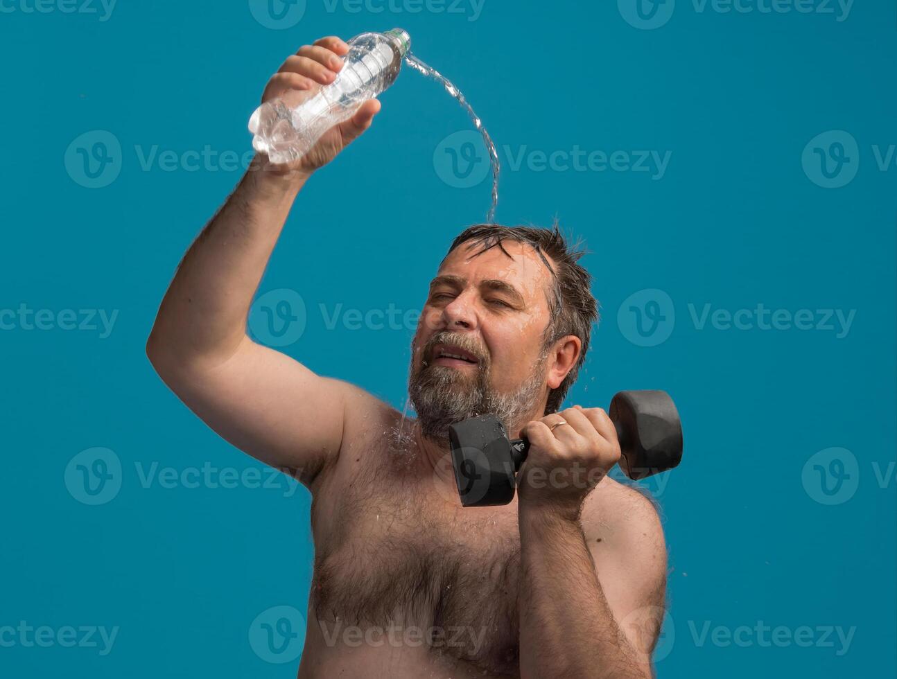 Elderly man lifting dumbbells while cooling off with water during workout session photo