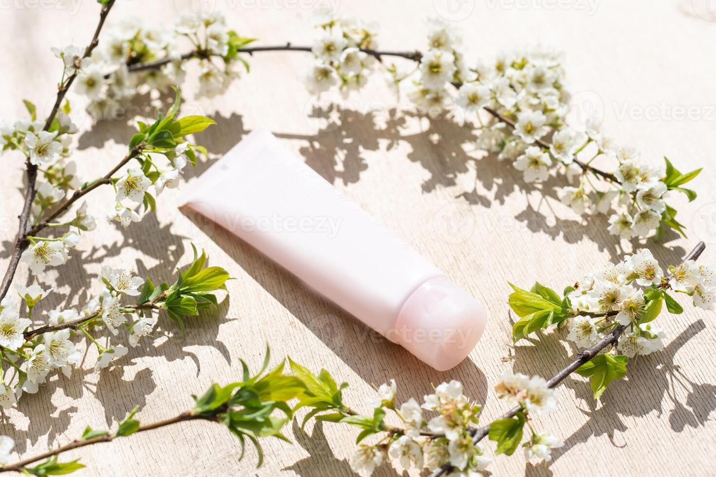 Blank white cosmetics tube and spring flowering tree branch with white flowers on pastel background. Front view photo