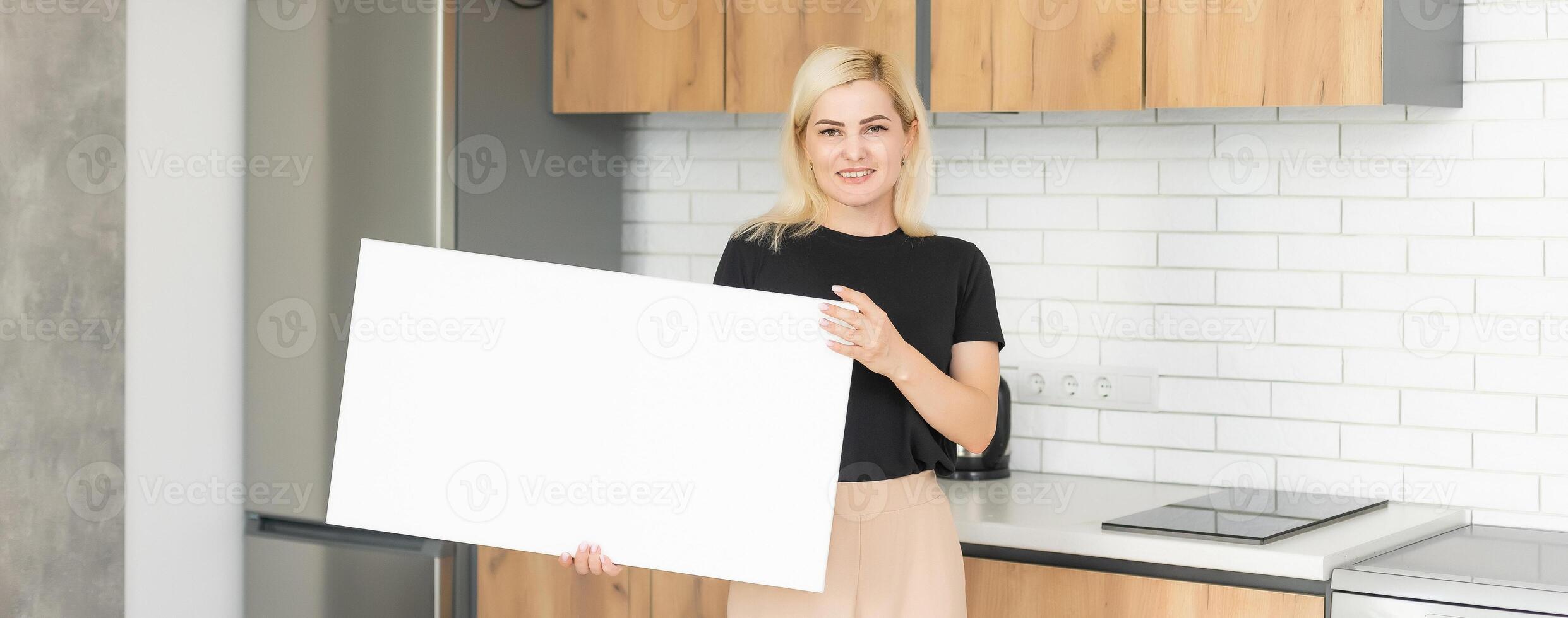 White canvas in female hands with gray wall background. Woman hanging blank picture mockup on wall with sconce. Wall decor. Canvas stretched on frame. photo
