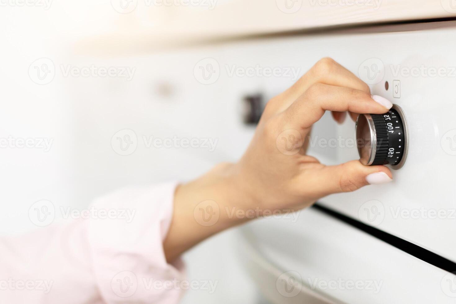 Closeup of female hand touching and turning knob, using stove in modern kitchen at home, controlling temperature of the burner, preparing meal, cooking food at home, selective focus on button photo