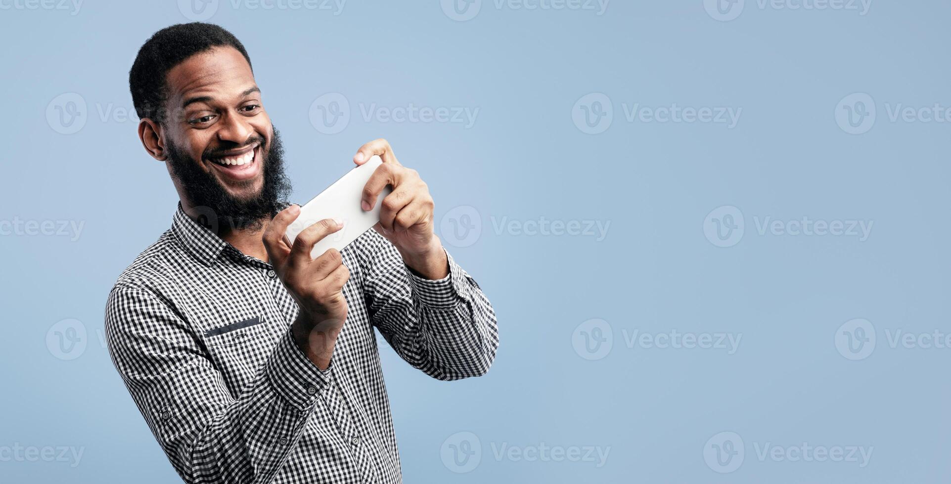 Portrait of excited african man playing games using cell phone isolated over blue background, copyspace photo