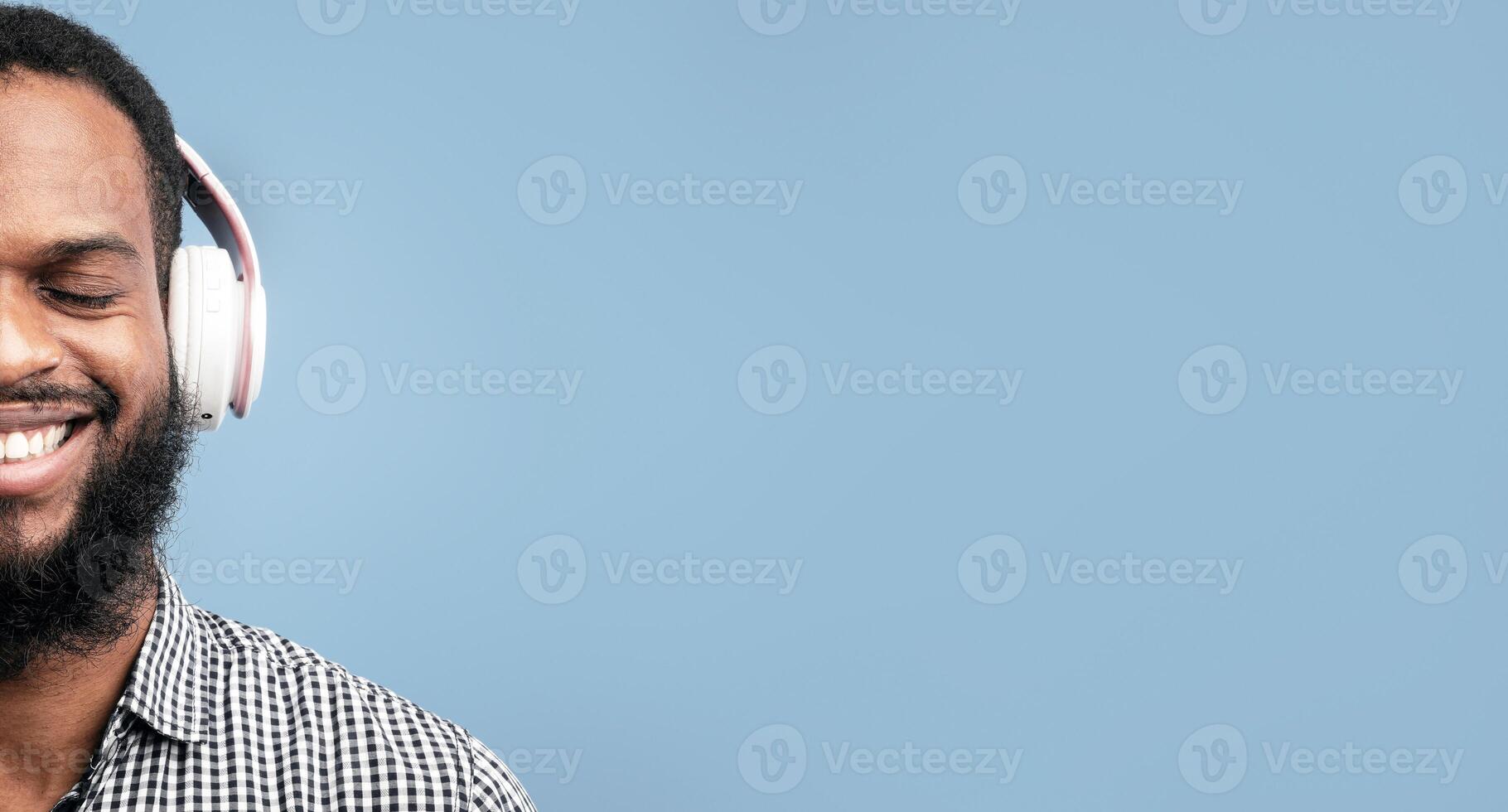 Perfect Song. Closeup portrait of smiling african guy listening to music or podcast in headset isolated on blue studio wall photo