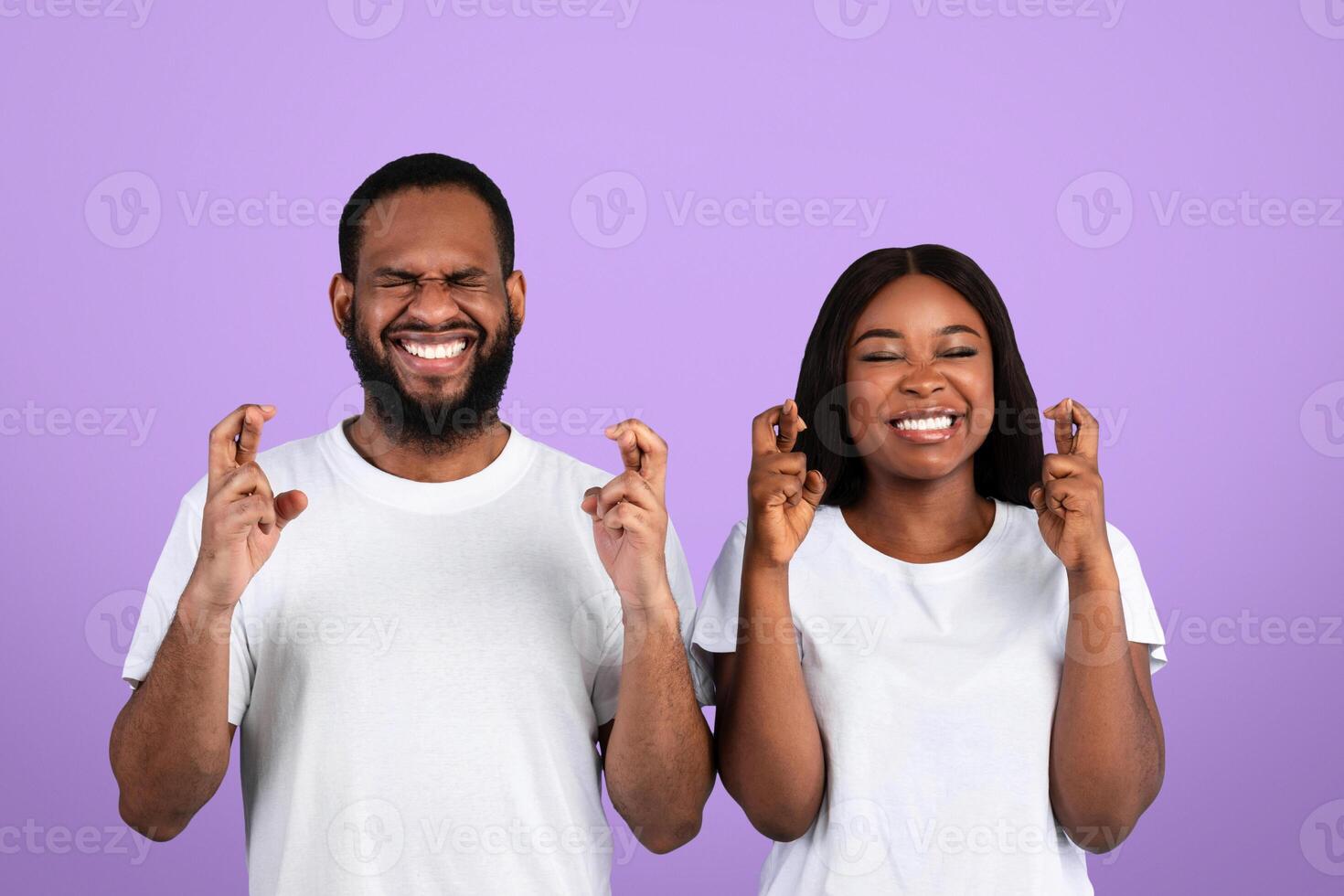 Luck And Superstition Concept. Cheerful millennial black couple gesturing and crossing fingers in hope, anticipate something with faithful expressions and closed eyes, isolated on blue background photo
