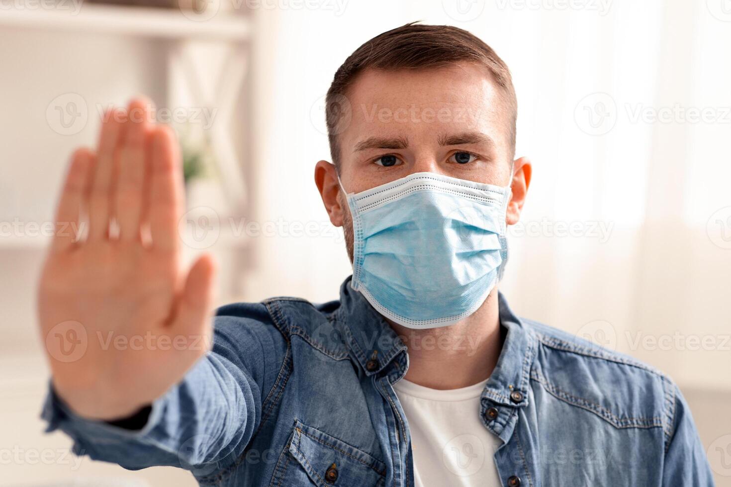 Stay at home. Young man in protective mask gesturing stop on camera photo
