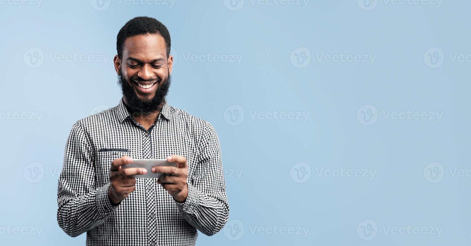 Gaming Concept. Smiling black guy using cellphone, browsing internet and chatting, turquoise wall, copyspace photo