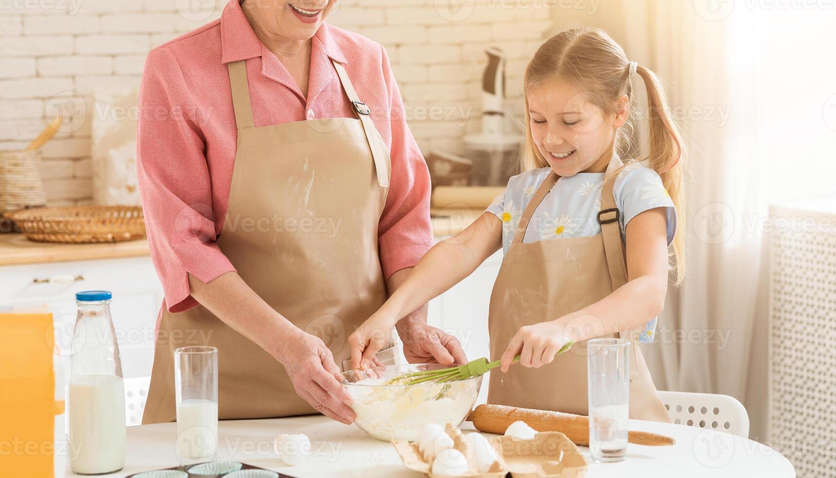 Baking with granny is fun. Older woman and her granddaughter mixing dough for pastry together in kitchen, copy space photo