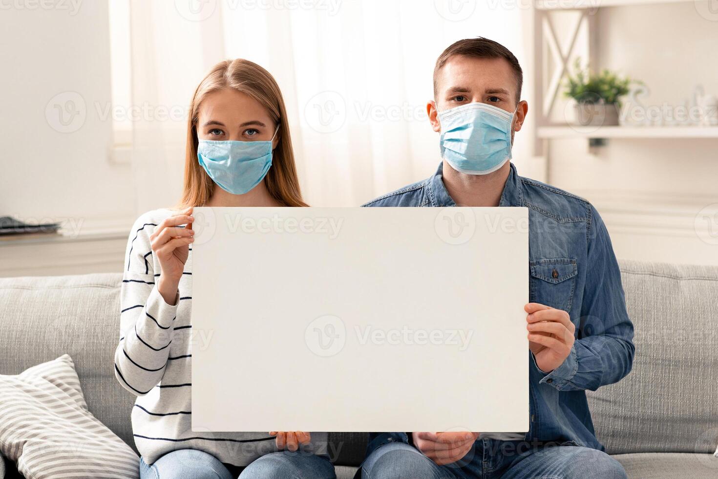 Global quarantine concept. Self-isolated couple in protective masks holding blank placard, free space photo