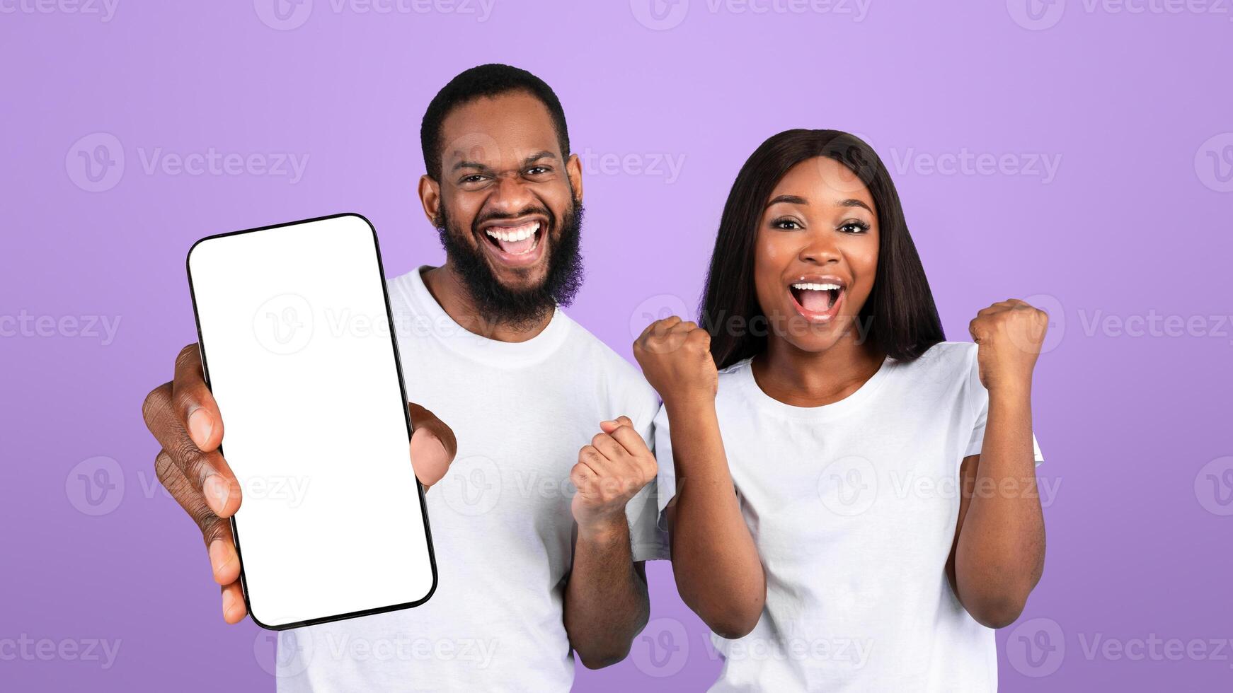 Big Win Concept. Excited young African American couple cheering and raising hands, celebrating victory. Emotional happy man and woman posing and shaking clenched fists, blue studio background, banner photo