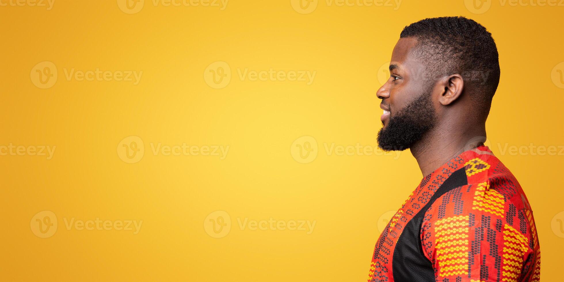 Profile photo of young african man in colorful shirt looking at copy space over yelllow