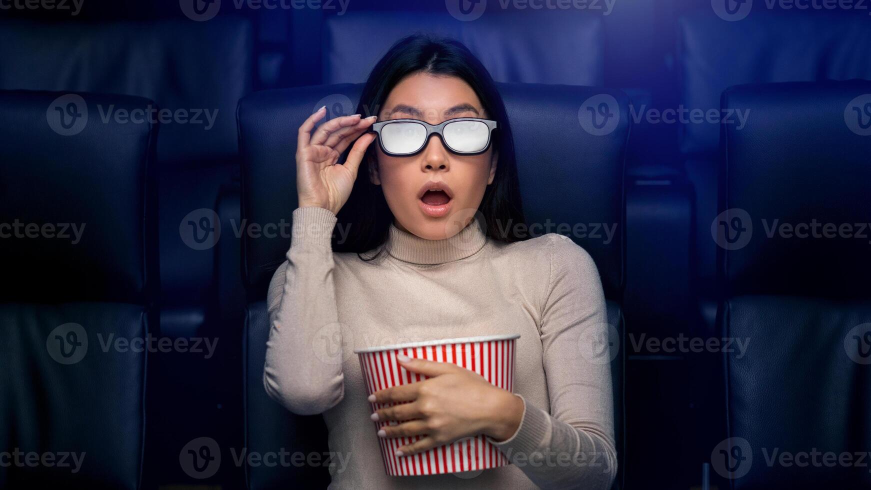 Scared Asian woman in 3D glasses watching horror movie in cinema photo