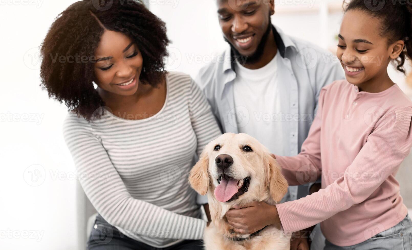 Happy Loving Family. Portrait of smiling black man, woman and girl hugging and stroking their happy dog sitting on the floor carpet in living room at home, playing with adopted domestic animal photo