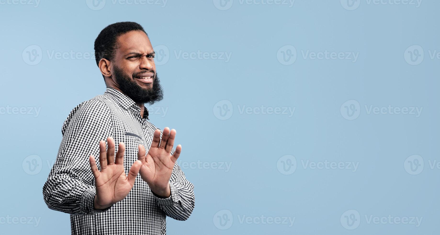 Keep Distance. Displeased black guy with disgusted facial expression standing with raised hands over blue studio wall photo