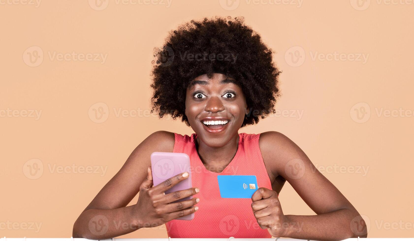 Mobile Shopping Application. Excited Black Lady Using Phone And Credit Card For Shopping Posing With Clothing Rack Over Yellow Studio Background, Smiling To Camera. photo