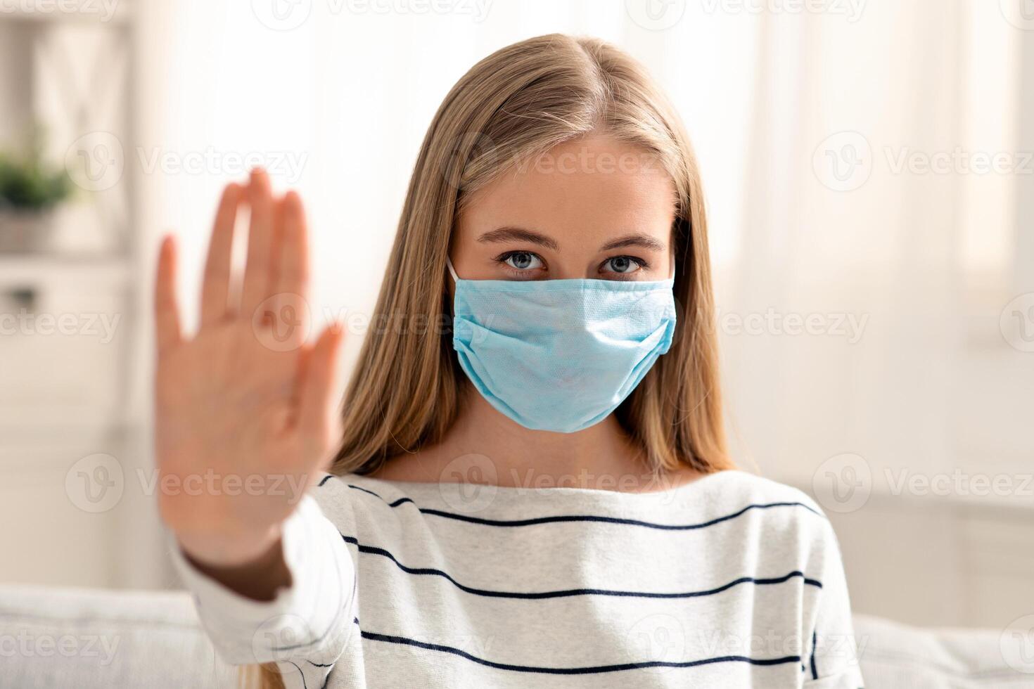 No contacts. Young woman in medical protective mask gesturing stop at home photo
