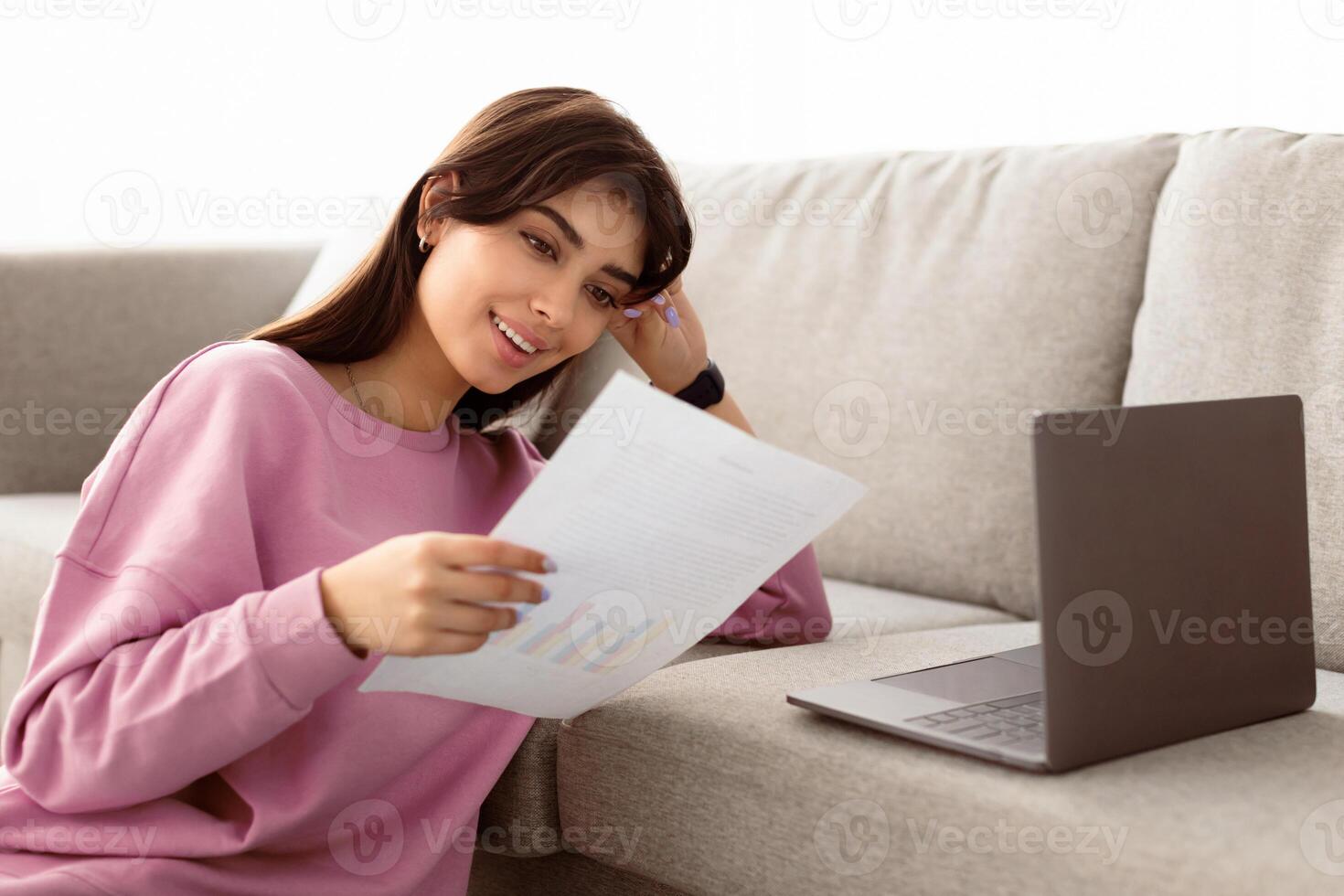 Young Female Self-Entrepreneur Working With Papers In Home Office, Checking Annual Financial Reports. Millennial Woman Reading Documents, Sitting On Floor With Computer, Leaning On Couch photo