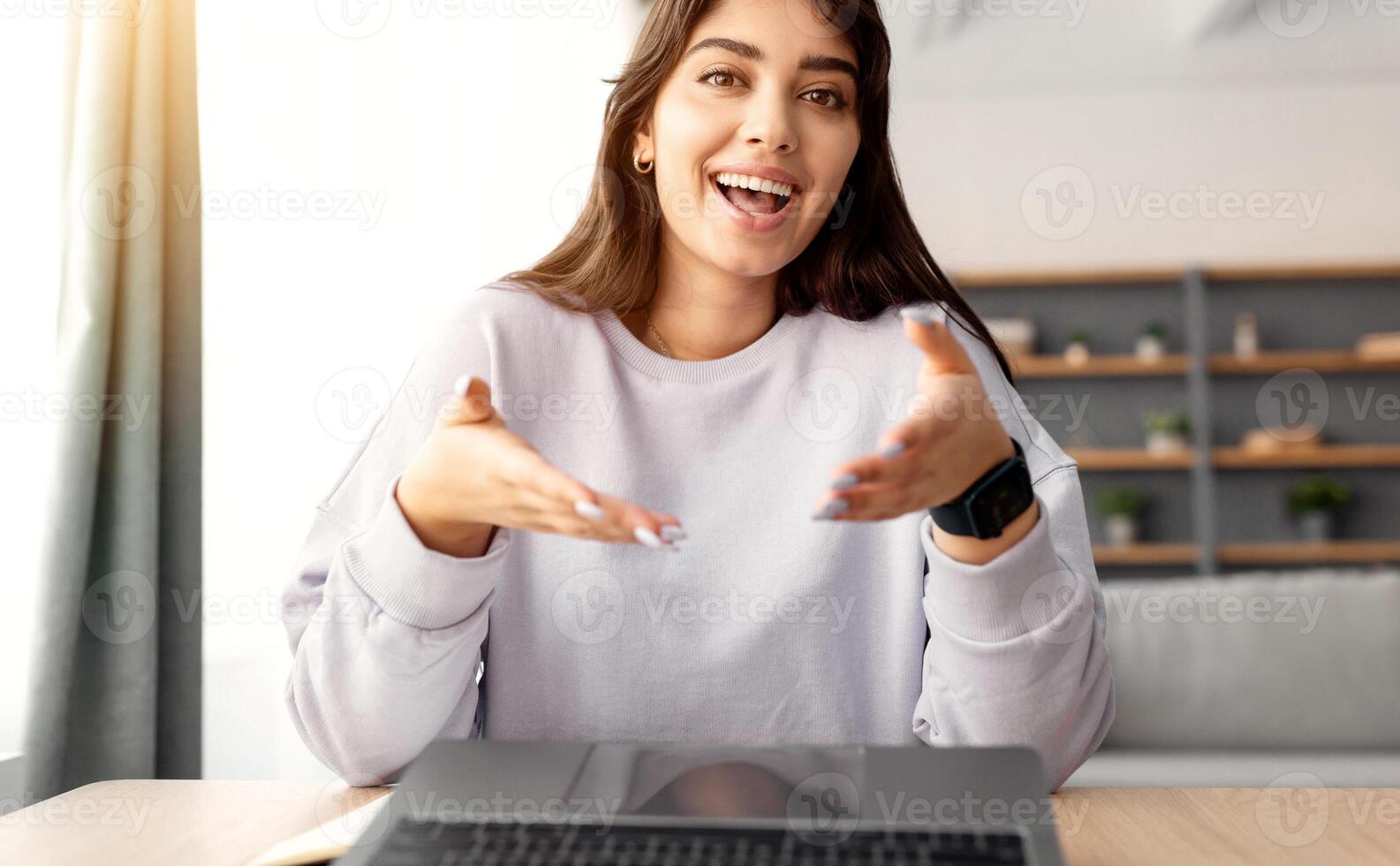 Online Call. Portrait of smiling young lady having virtual conference with friends, family or colleagues using computer, talking and gesturing to webcam, sitting at desk at home office photo