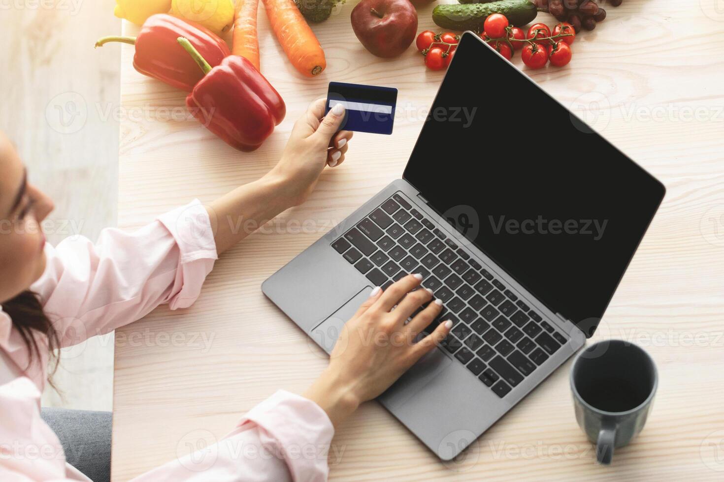 Easy Payment. Above top high angle view of smiling young woman using laptop sitting at dinner table, holding and showing debit credit card. Housewife ordering food, free copy space photo