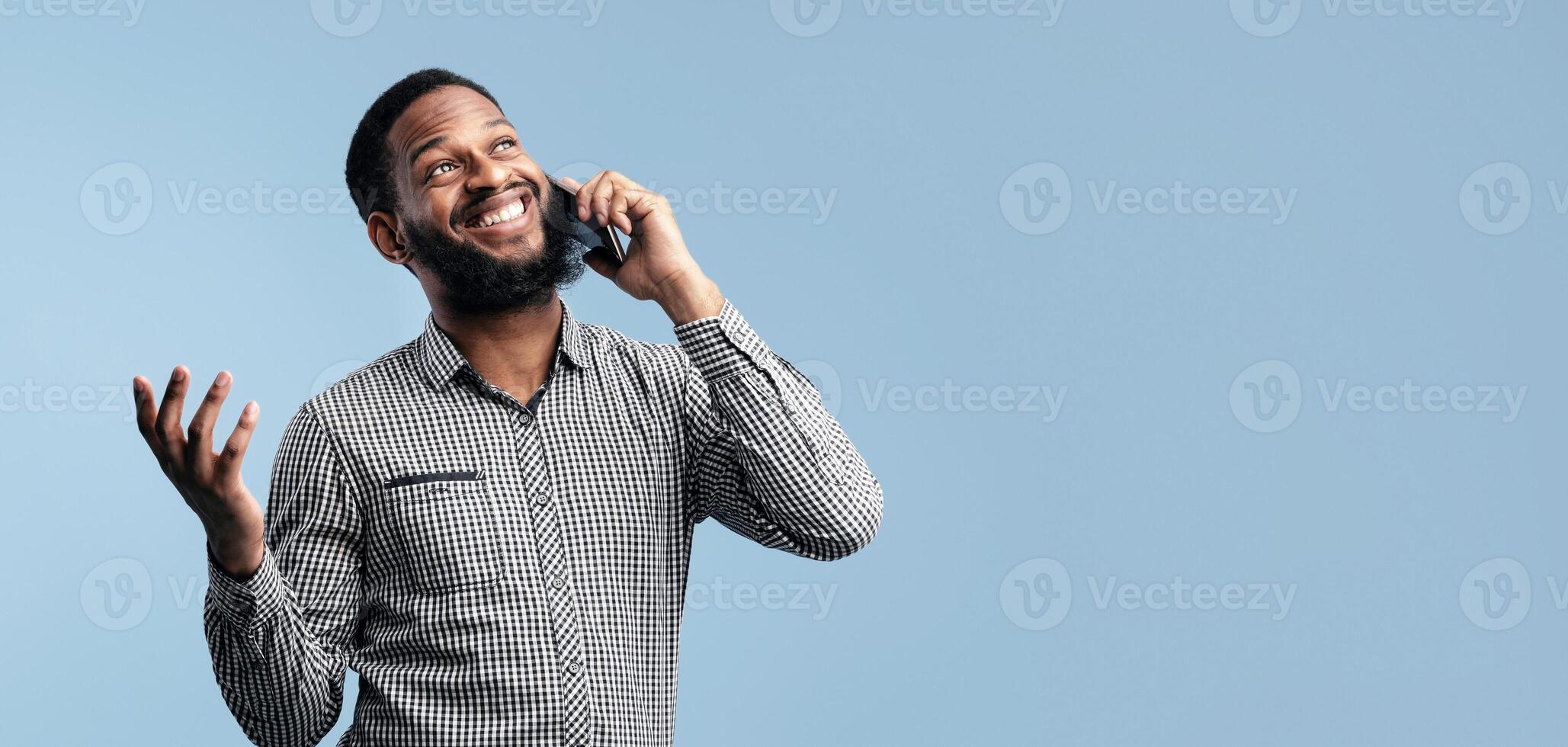 Phone Talk. Happy African Guy Chatting On Cellphone Standing And Gesturing Over Blue Studio Background, Isolated photo
