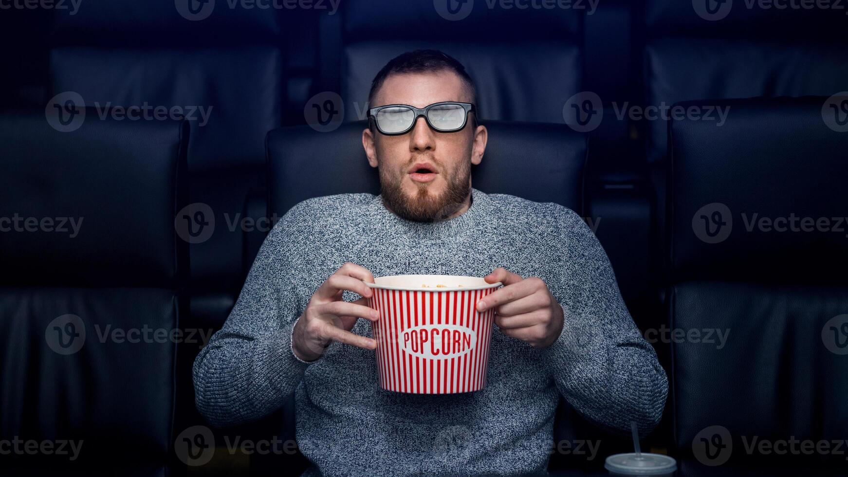 Alone in empty cinema. Scared young man with popcorn watching 3D thriller in movie theater photo
