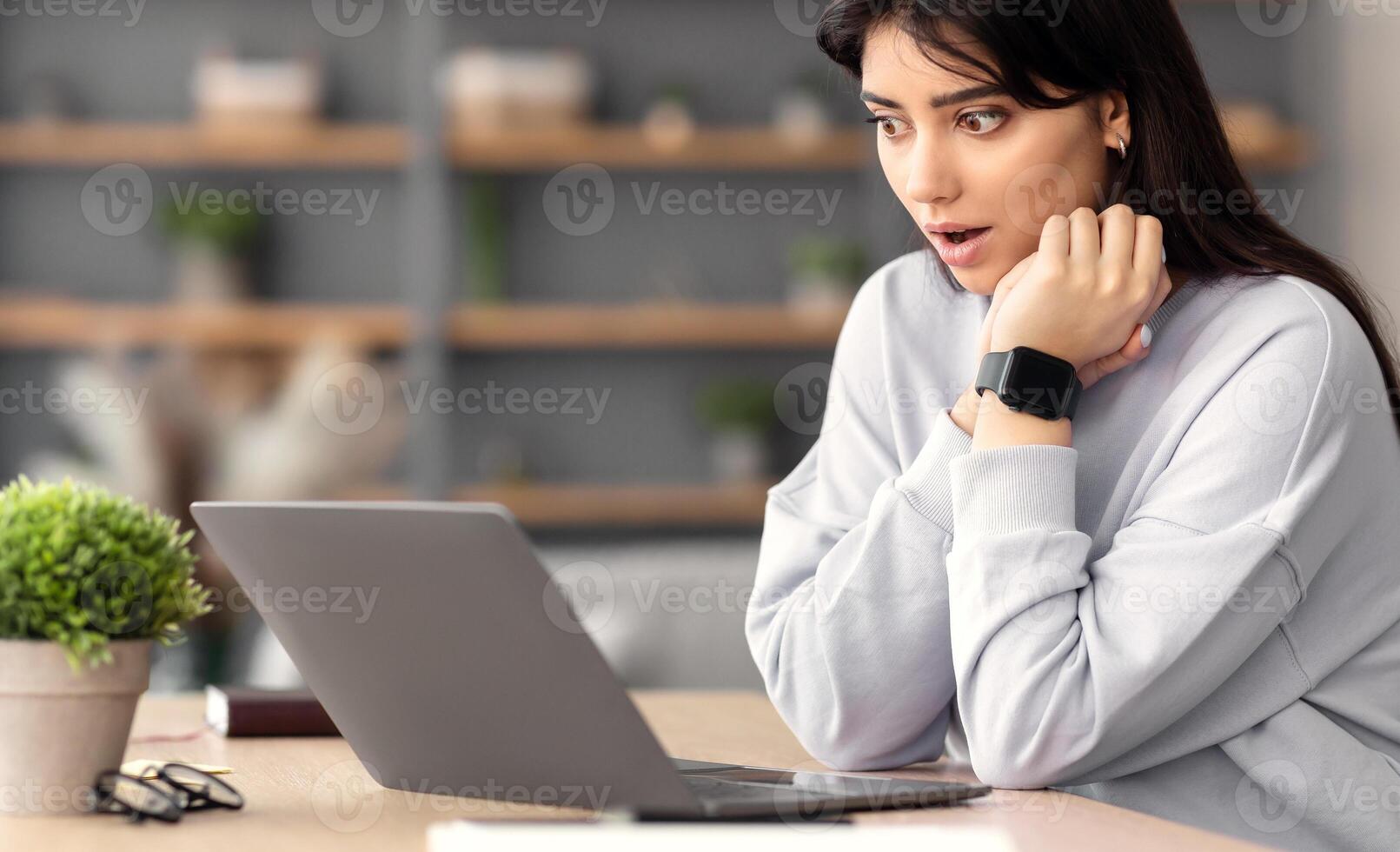 Omg, Breaking News. Shocked asian woman watching something surprising and unexpected on laptop, sitting on couch at home, copy space. Portrait of young lady with open mouth in amazement photo