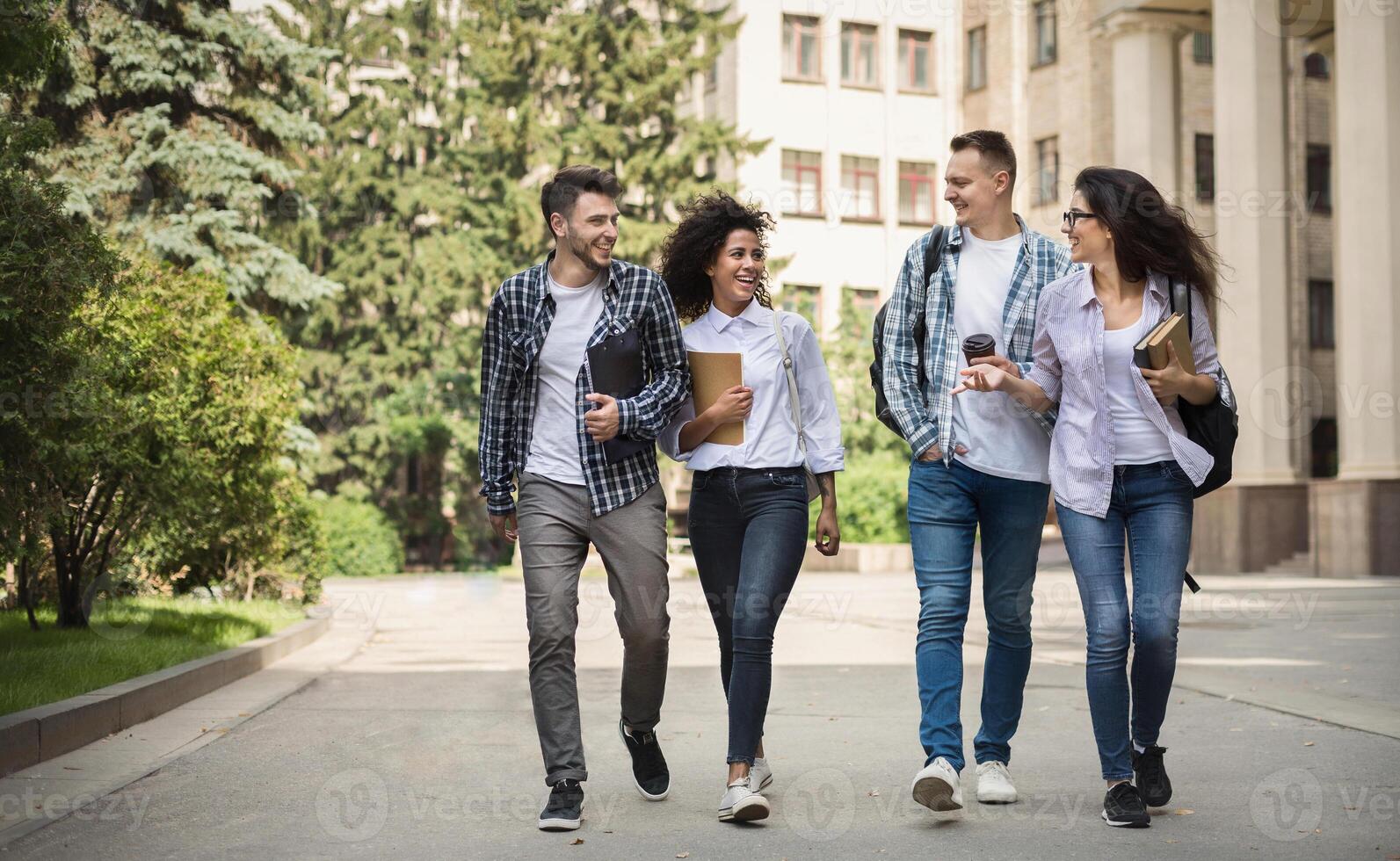 Multiethnic group of smiling students walking together walking near college photo