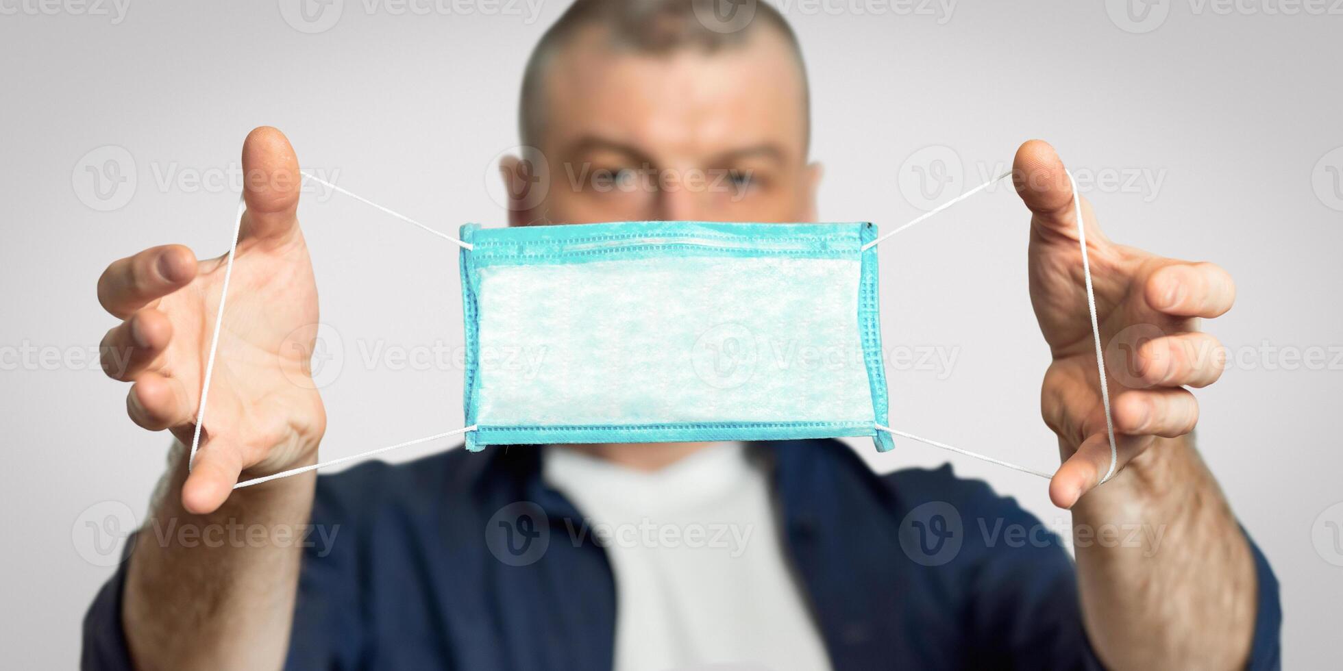 Coronavirus Protection. Man Showing Medical Mask To Camera Standing On Gray Studio Background. Shallow Depth, Panorama photo