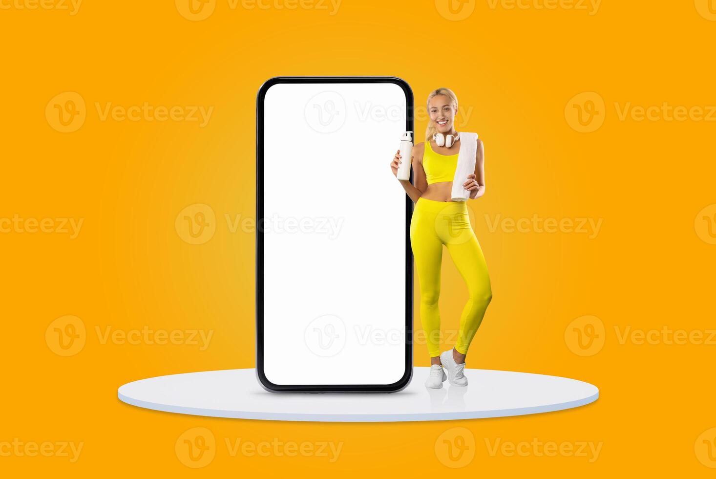 A cheerful young woman dressed in bright yellow athletic wear holds a smartphone and stands beside a large, empty smartphone display. The background is bright and engaging. photo