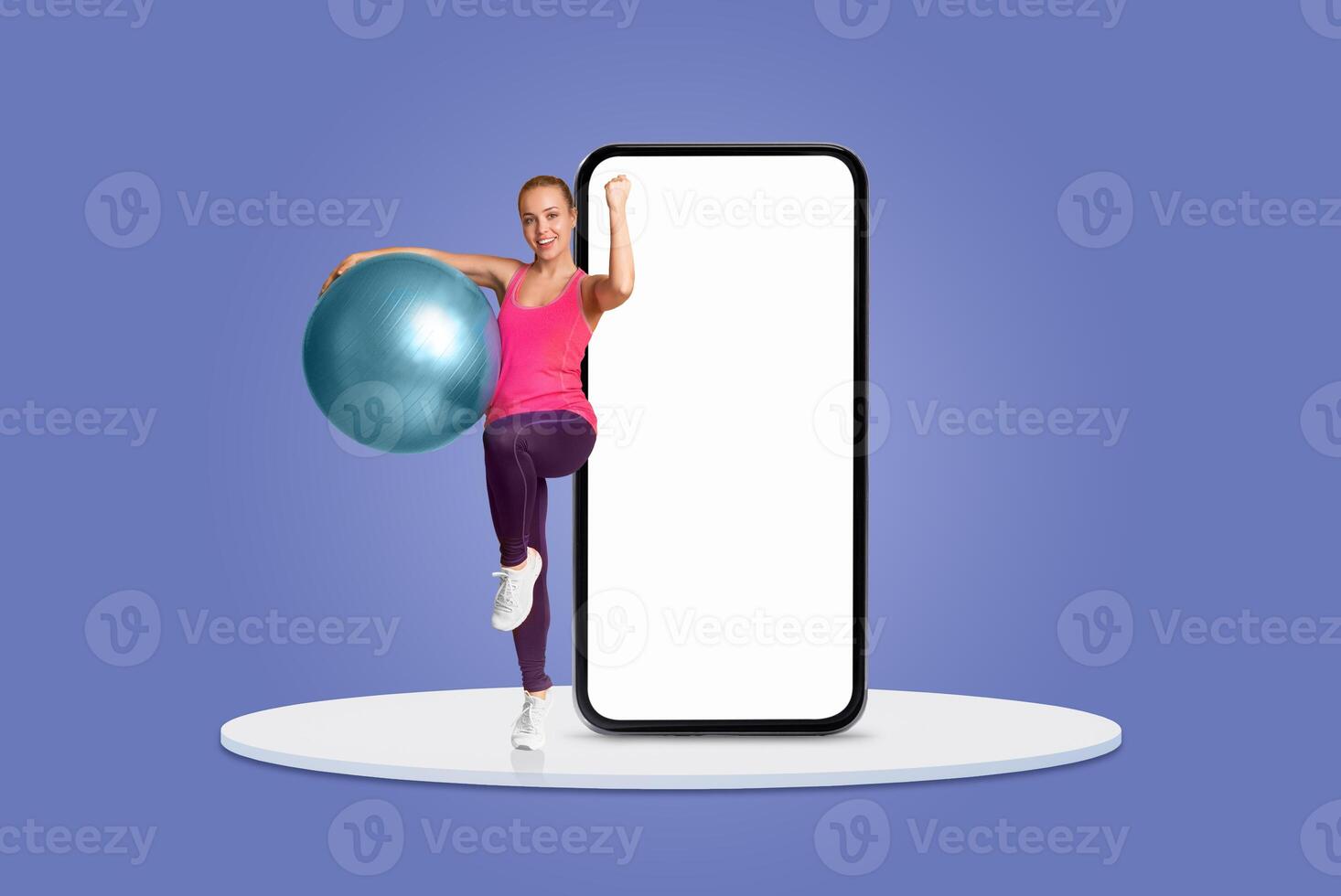 A woman in activewear confidently demonstrates an exercise routine using a fitness ball, while a large blank smartphone screen serves as a backdrop, creating an energetic atmosphere. photo