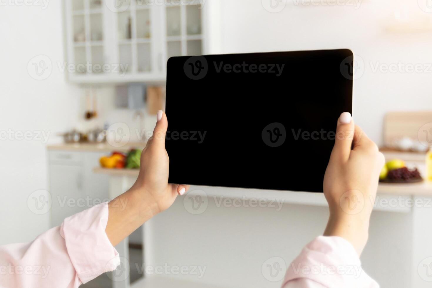 Over the shoulder view of young woman holding digital tablet with black empty screen for mockup template, standing at modern kitchen. Technology, Template, Automation, Smart Home Concept photo