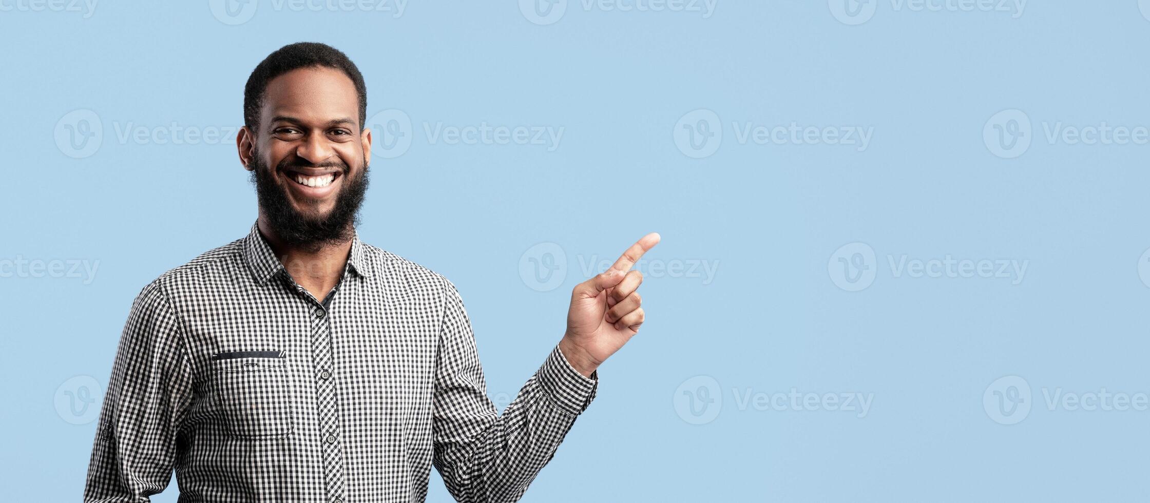 Cool Offer Concept. Portrait Of Smiling Young Black Bearded Man Pointing Finger At Copy Space Isolated Over Blue Background. Cheerful Confident African American Guy Indicating Free Space, Banner photo