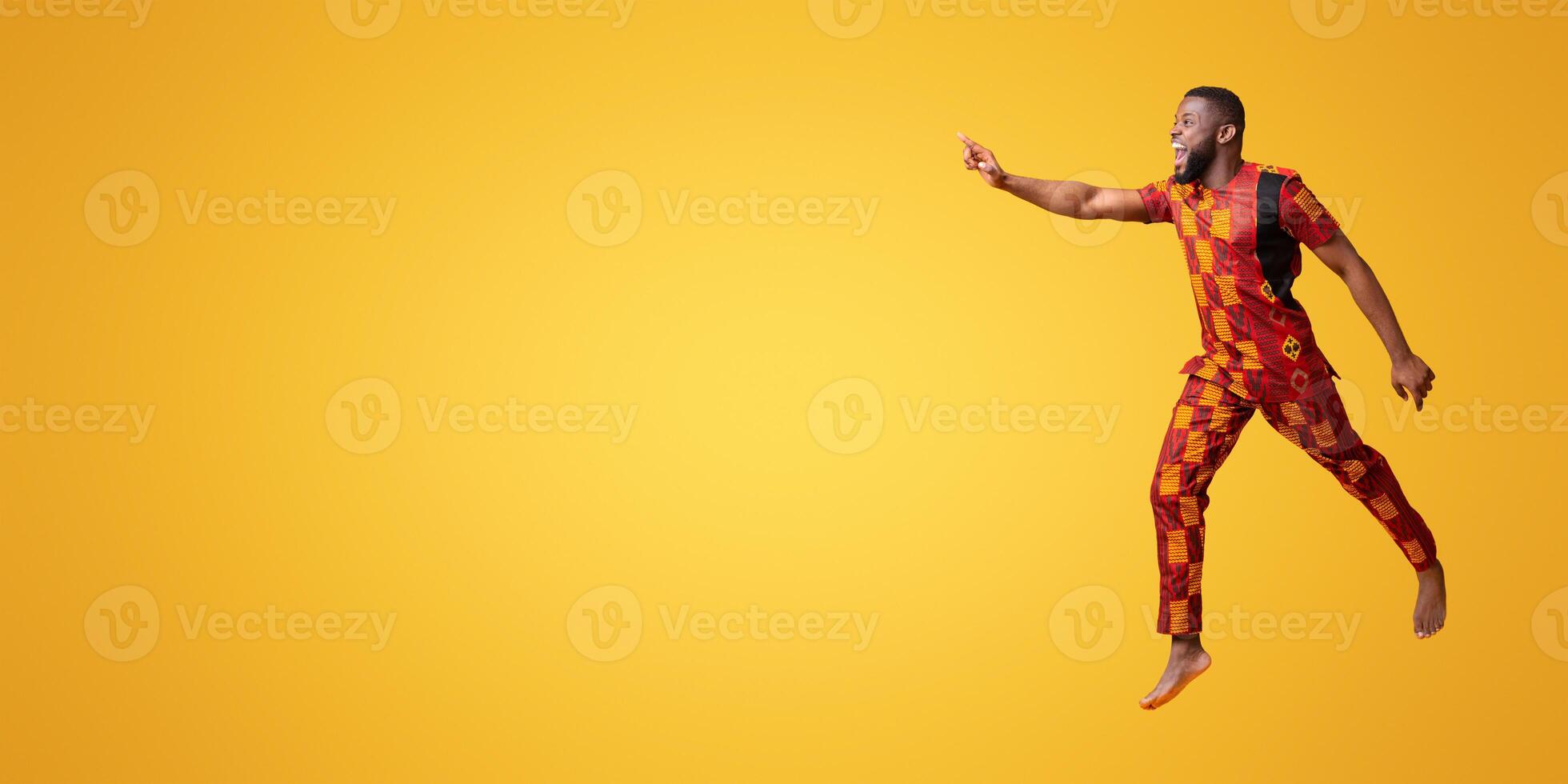 Excited black man in colorful authentic costume running towards copy space for advertisement, yellow background photo