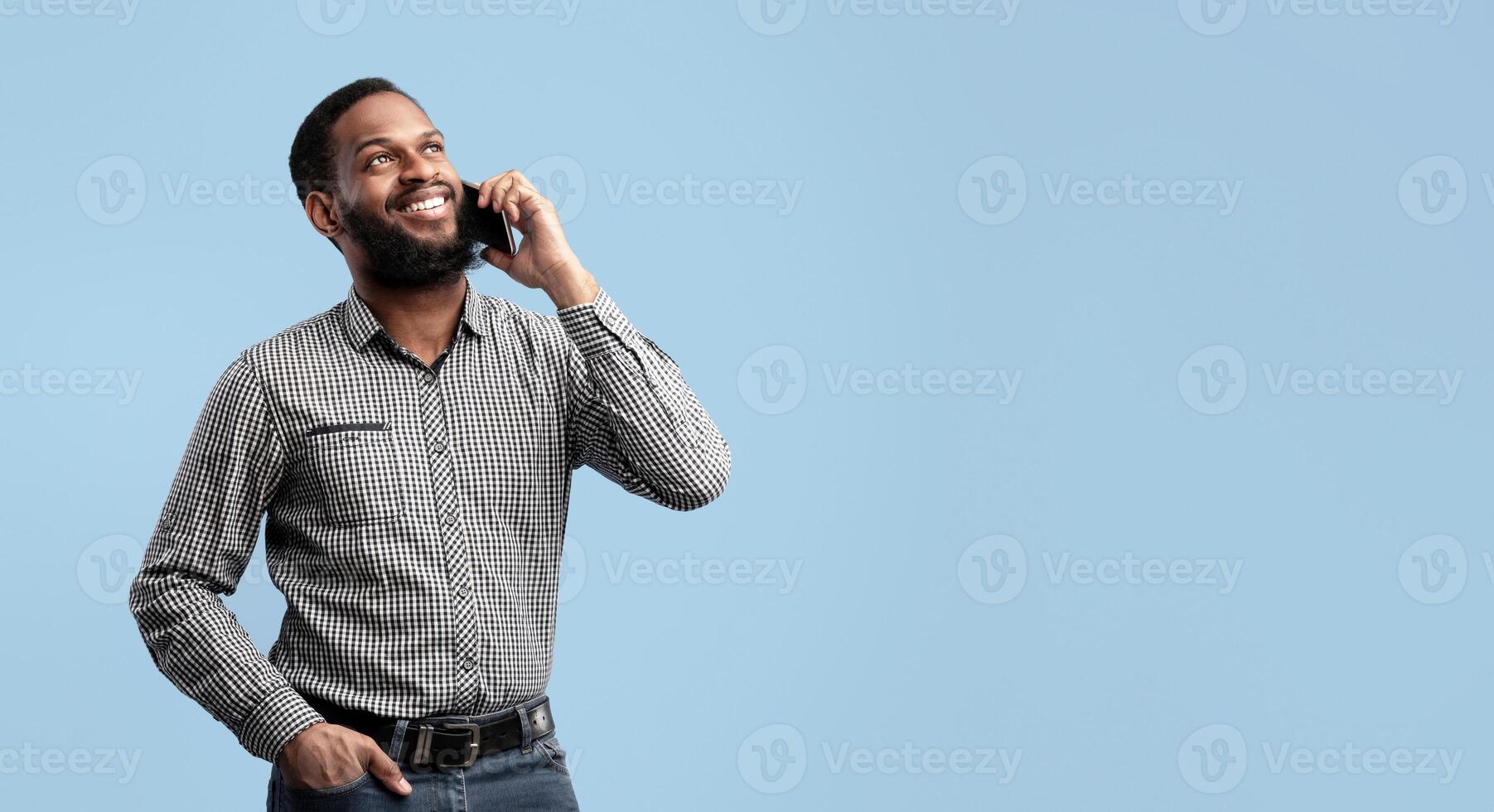 Corporate Communication. Portrait Of Happy African American Executive Making Business Call Standing Isolated Over Blue Studio Background. Bearded Black Man Talking On Cellphone, Looking Up, Copy Space photo