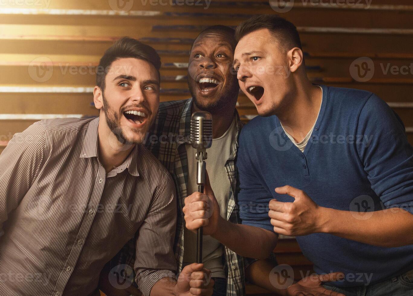 Happy male friends singing karaoke together in bar photo