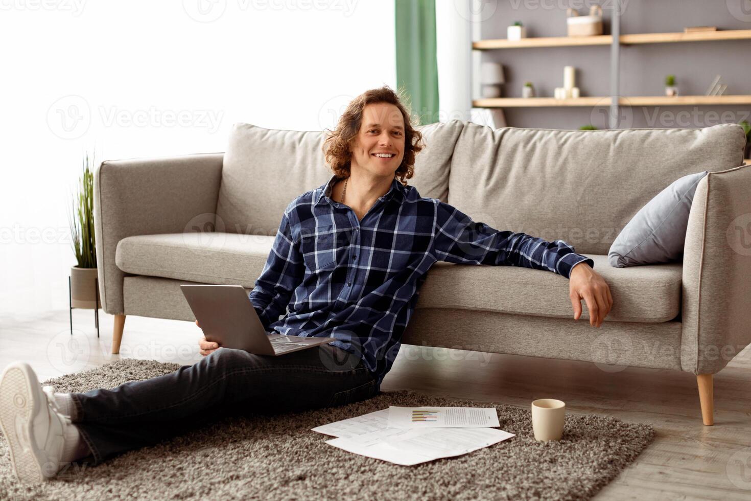 Distant Work. Successful Freelancer Man Posing With Laptop Sitting On Floor And Smiling To Camera Working Online From Home. Internet Technology, Freelance Career And Lifestyle Concept photo