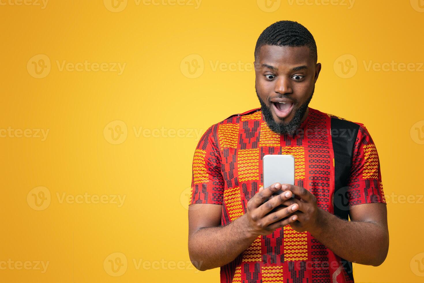 New mobile app. Amazed black guy in authentic t-shirt looking at smartphone screen over yellow background photo