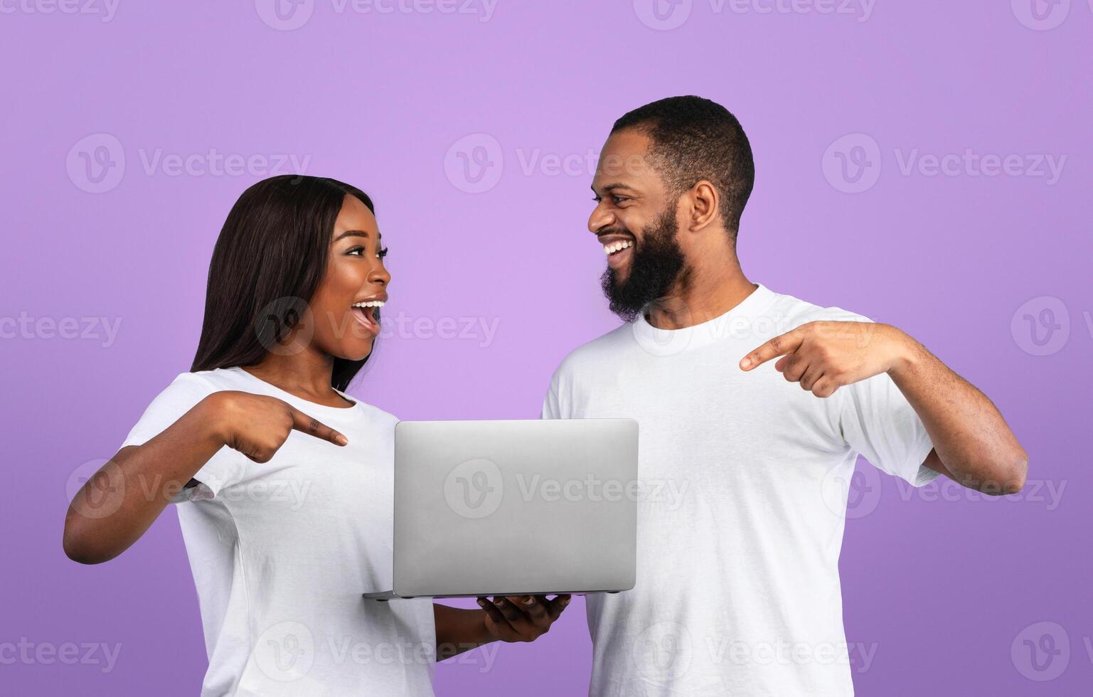 Online Life Concept. Happy black couple holding laptop, surfing web, watching movie, pointing at screen and looking at each other. People reading exciting news. Remote entertainment, work, education photo