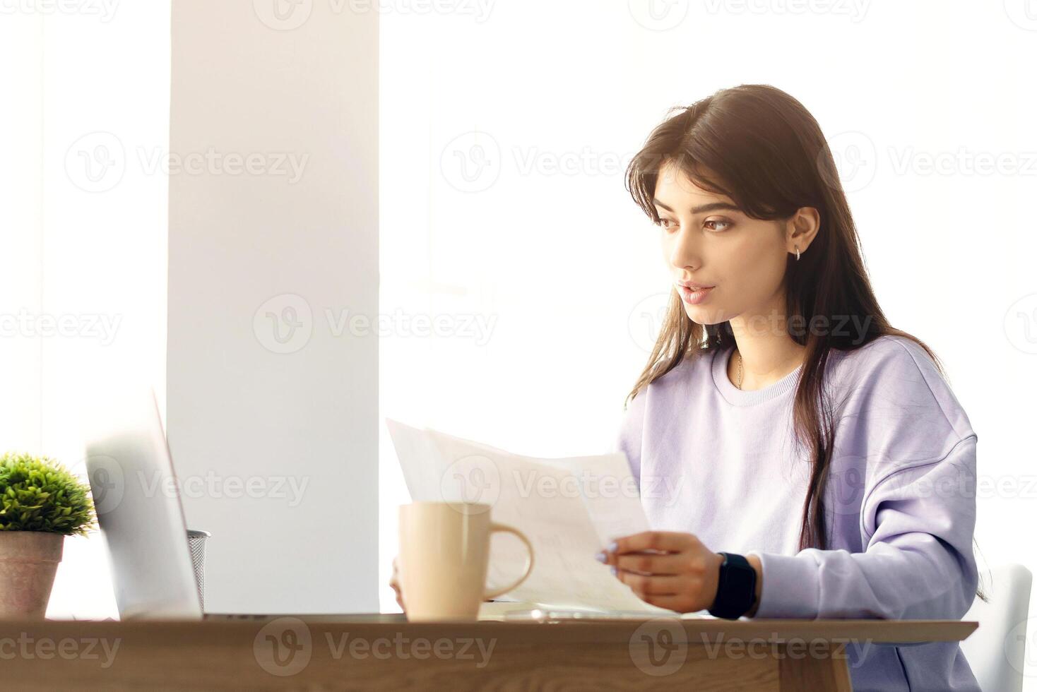 Young Female Manager Working With Papers In Home Office And Having Call On Laptop, Talking And Making Annual Financial Reports. Millennial Woman Holding Documents, Sitting At Desk With Computer photo