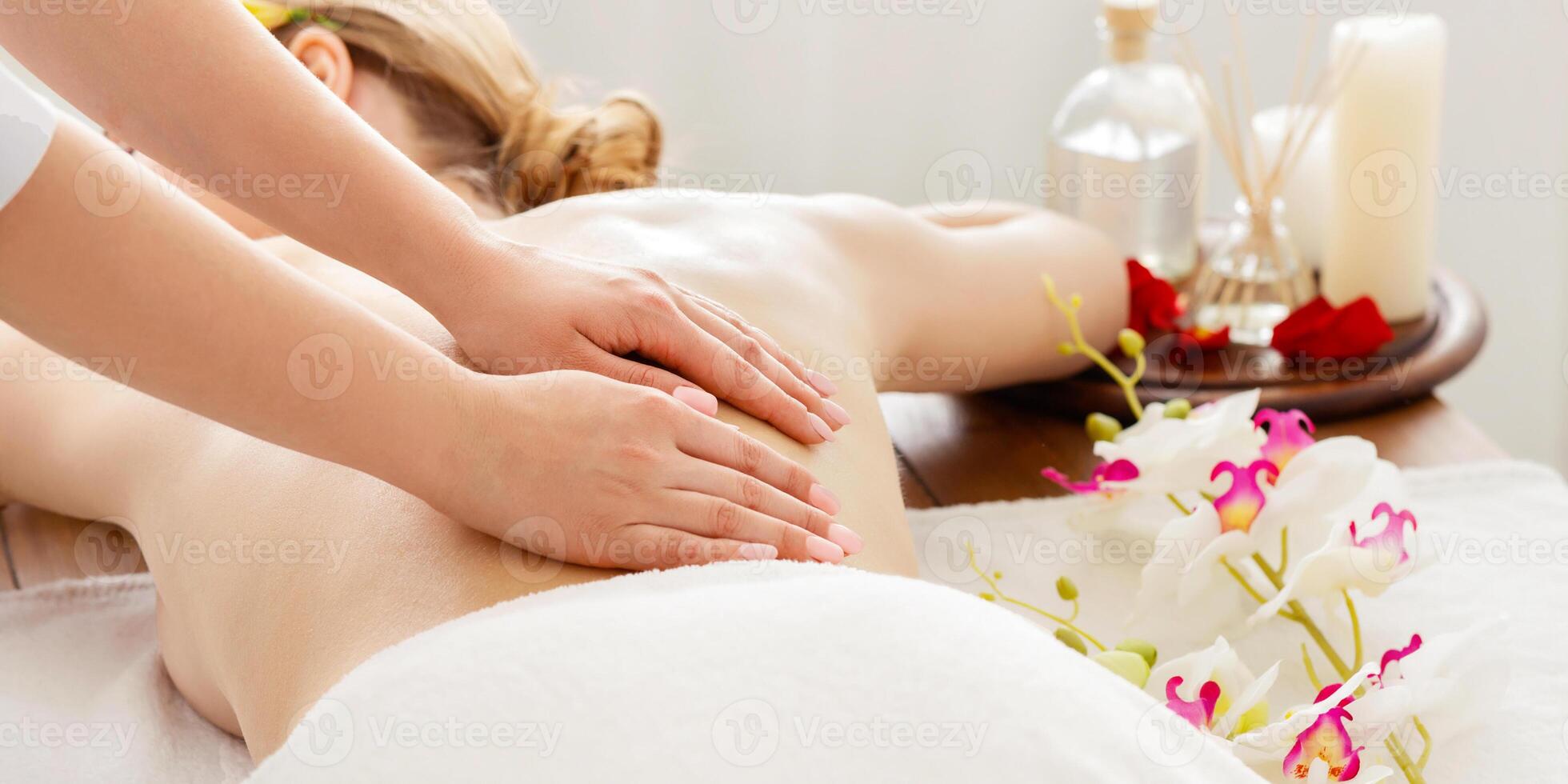 Spa day and aromatherapy. Girl receives massage on table with flowers, oil and aroma sticks photo