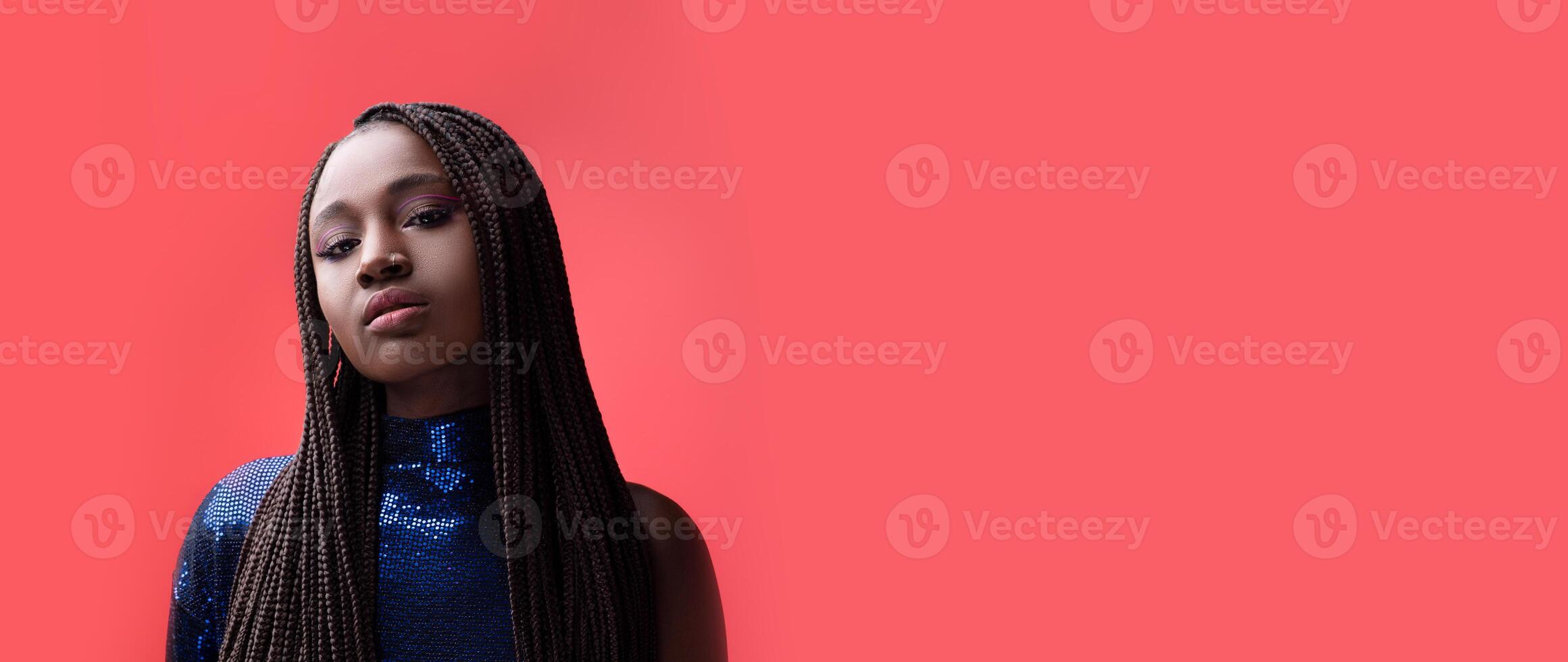 A black woman stands gracefully with a self-assured expression, her long braided hair framing her face. The vibrant coral background enhances the artistic charm of the moment. photo