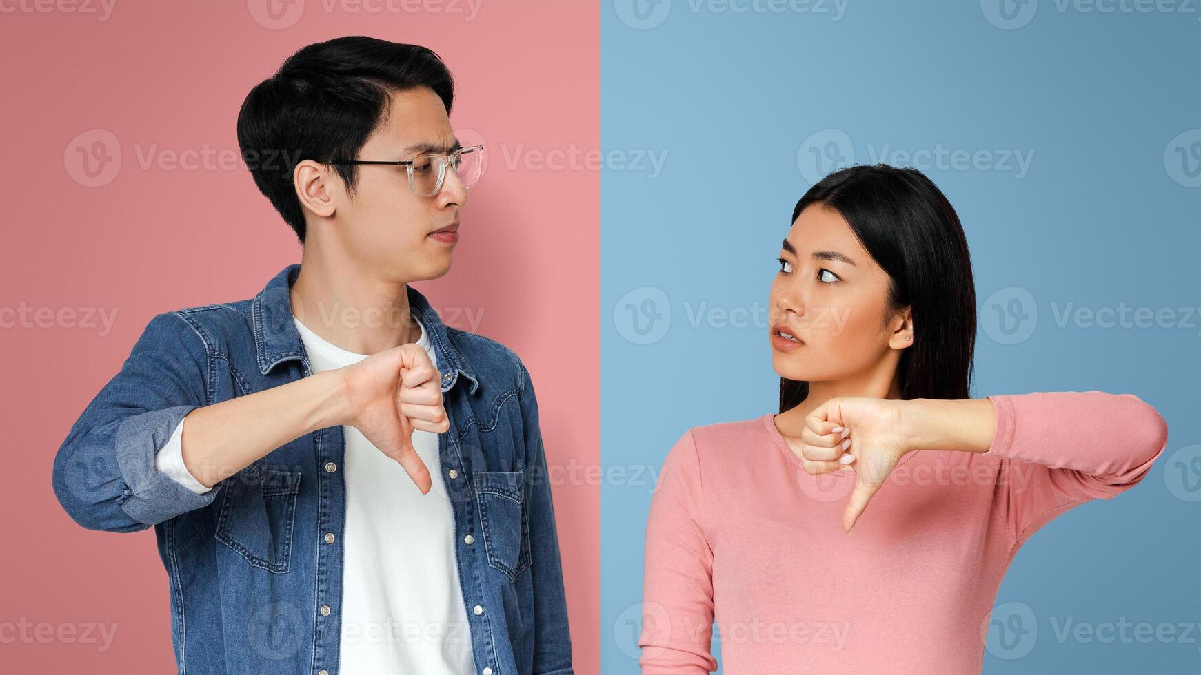 Something went wrong. Asian confused couple looking at each other with their thumbs down, grey background photo