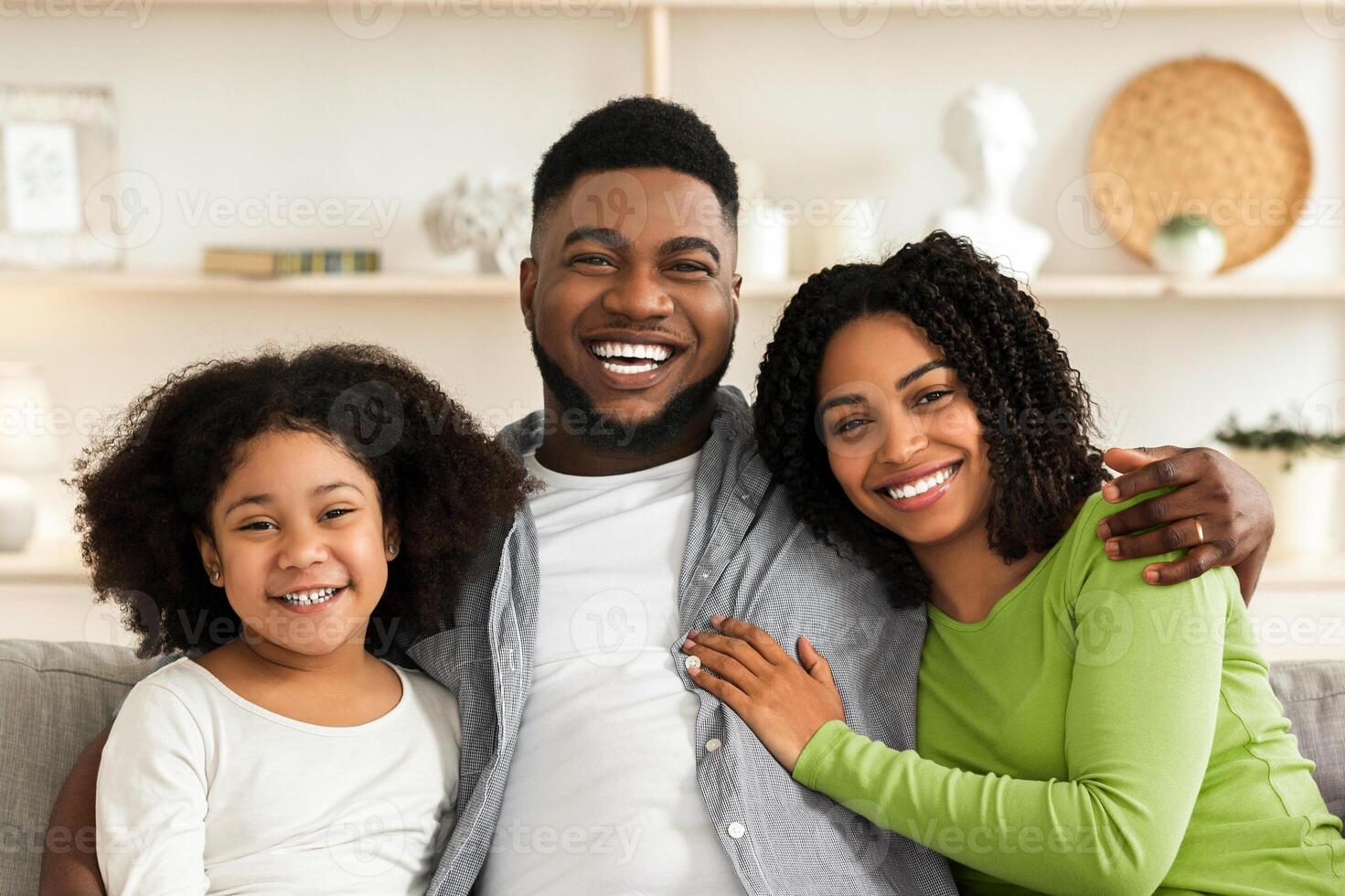Happy African American Family Of Three Posing At Home, Sitting On Couch, Embracing And Smiling photo