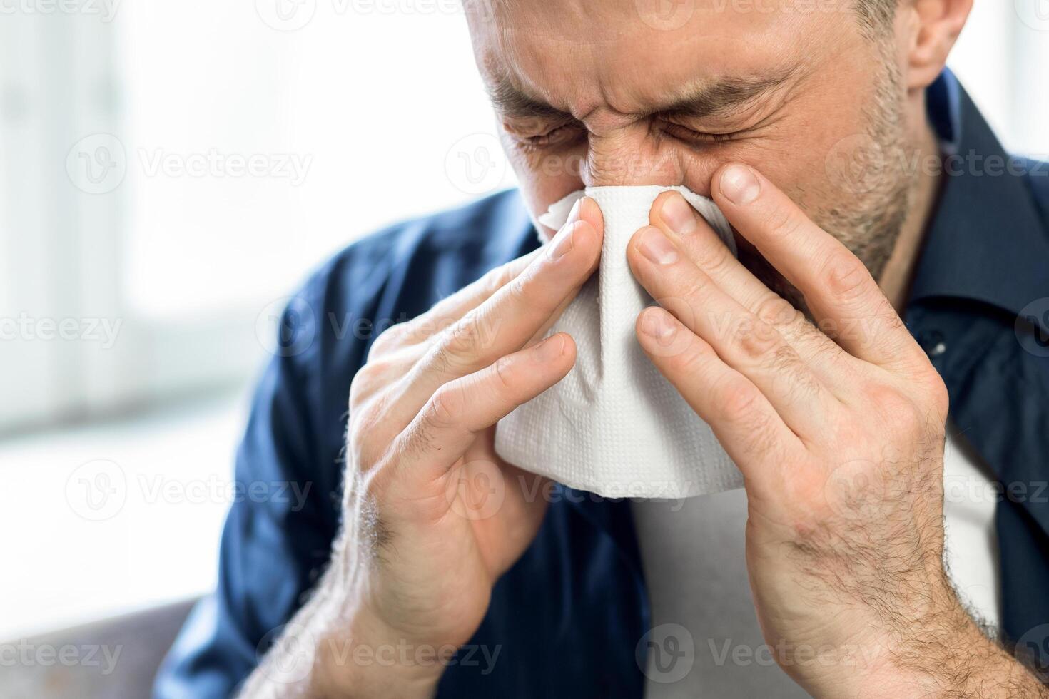 Coronavirus Concept. Sick Man Sneezing Blowing Nose In Paper Tissue Standing At Home During Covid-19 Pandemic Outbreak. Panorama, Selective Focus photo