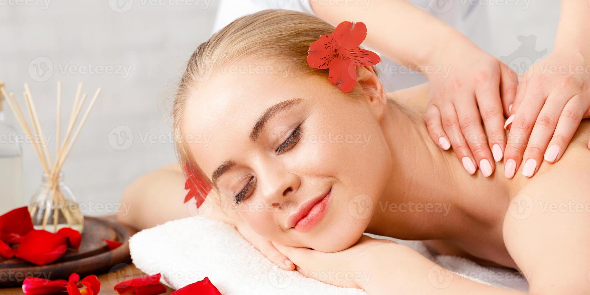 Relax, recovery and beauty care. Smiling girl lies on massage table with flower petals, aromatic sticks and oil photo
